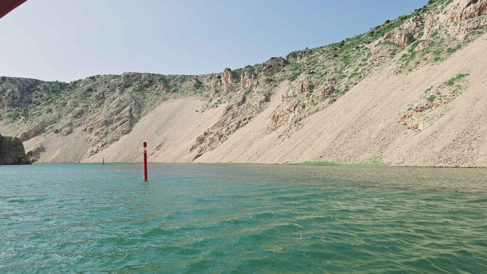 A calm lake with clear turquoise water, surrounded by rocky cliffs and sparse vegetation. 2
