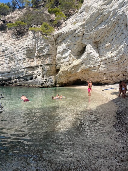 A rocky beach with clear water, people swimming and standing on the shore. 3