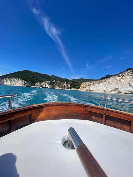 A boat on a clear blue sea with white cliffs and green hills in the background. 4