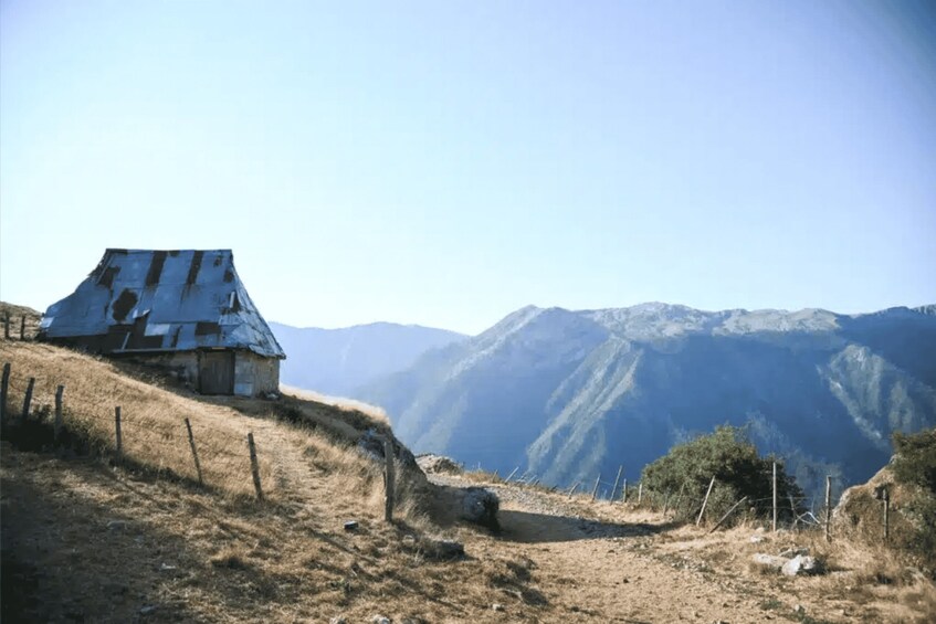 A rustic house on a hillside with a mountainous backdrop. 1