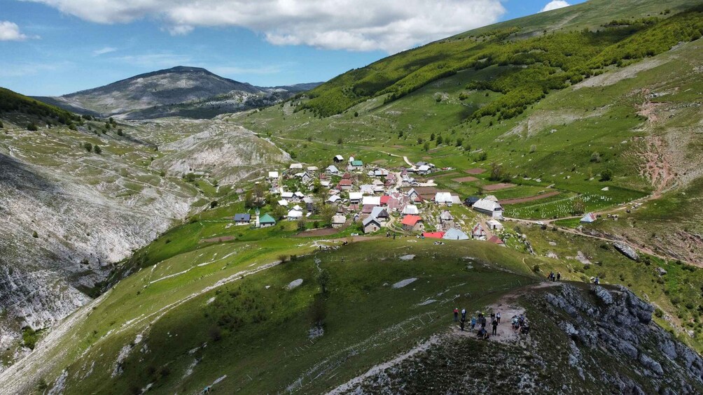 A village nestled in a valley with green hills and a mountain in the background. 1