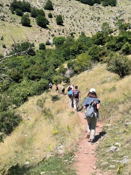 A group of hikers on a dirt trail surrounded by dry grass and scattered trees. 5