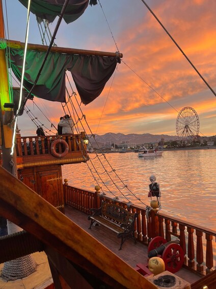 A wooden ship deck with a life preserver, a bench, and a skeleton figure. In the background, a Ferris wheel and mountains are visible. 2