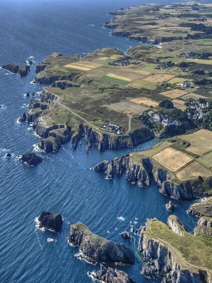 A coastal landscape with rocky cliffs, fields, and a winding road along the coastline. 3