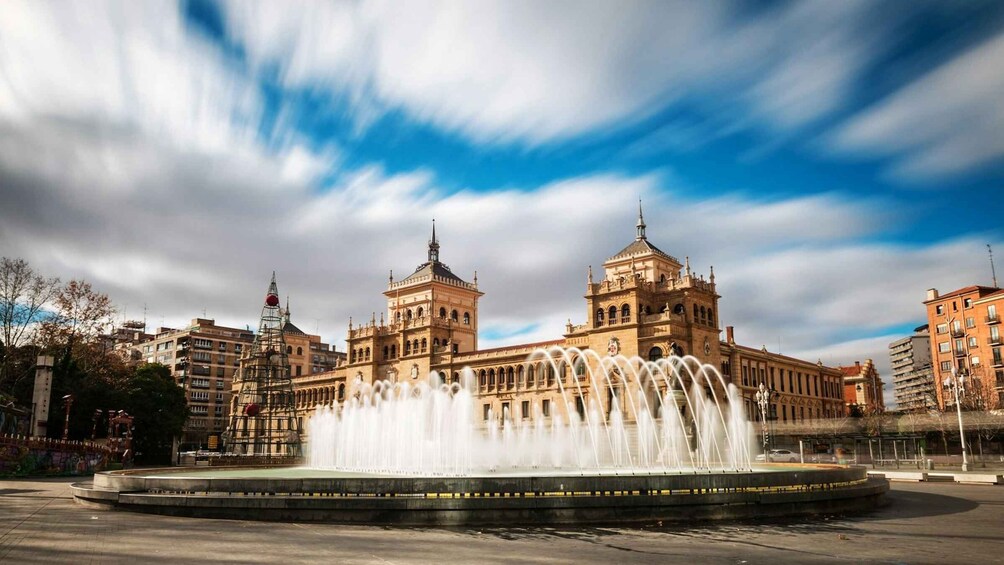 A historic building with two towers and a fountain in front. 1