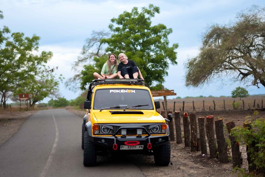 A yellow off-road vehicle with two people on the back, parked on a rural road with trees and a fence on the side. 5
