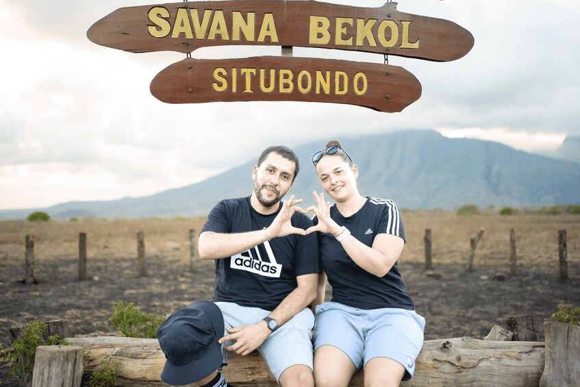 Two people sitting on a wooden bench with a sign above them that reads 'SAVANA BEKOL SITUBONDO'. 3