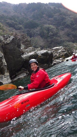 A person kayaking on a river with rocky banks and a forested hillside in the background. 2