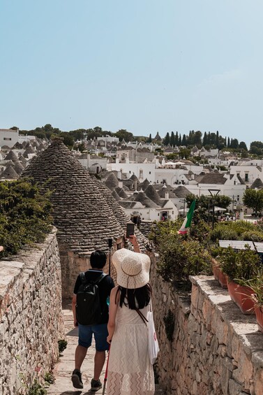 A couple walking on a stone pathway with a view of a village with conical-roofed buildings. 3