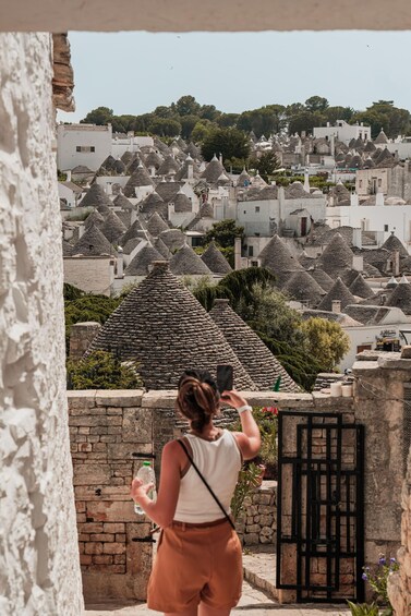 A woman taking a photo of a village with conical-roof buildings. 4