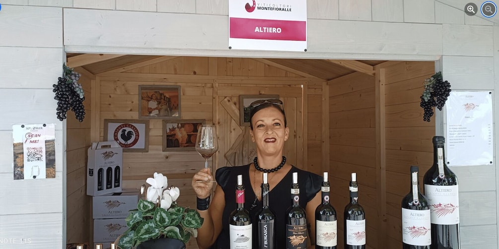A person holding a wine glass in front of a wooden wine cellar with several bottles of wine labeled 'Altiero' and a sign reading 'Altiero Montefiore.' 5