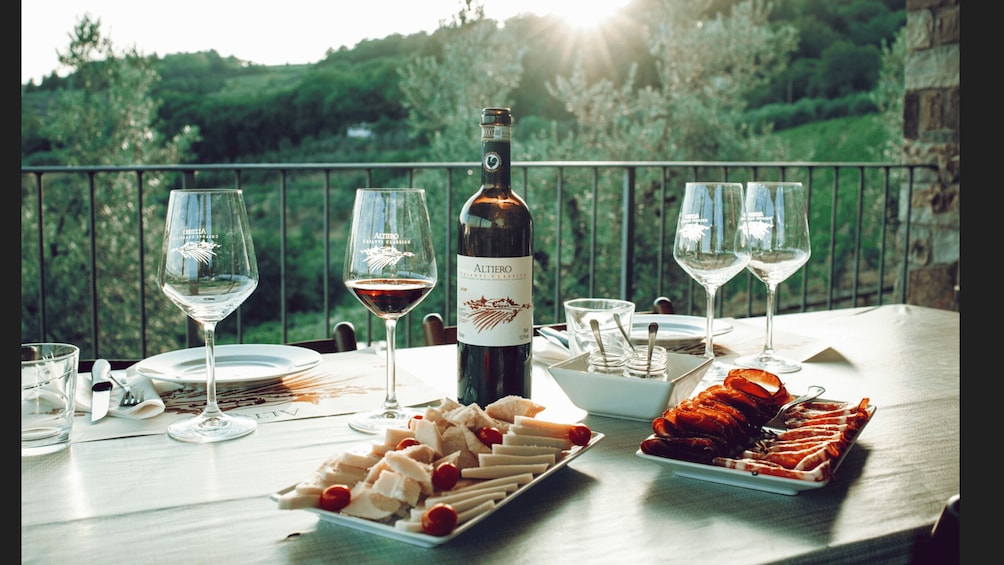 A table set with wine glasses, a bottle of wine, and a platter of food on a balcony with a scenic view. 3