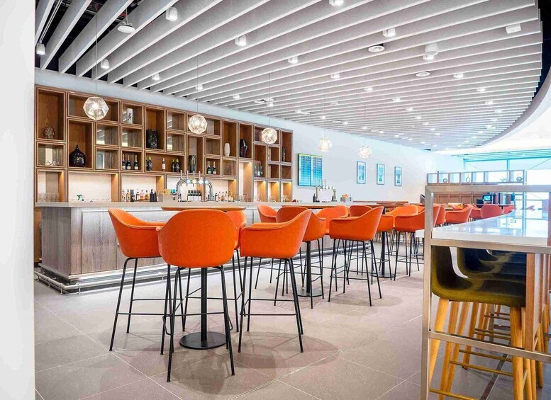 A modern bar with orange chairs, wooden shelves, and a unique ceiling design. 2