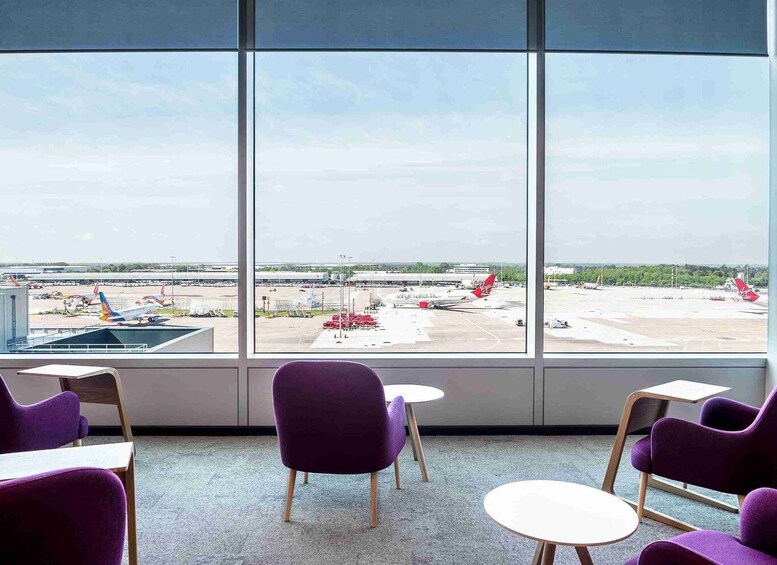 A room with purple chairs and a table, large windows with a view of an airport. 5