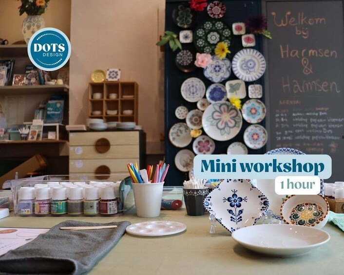 A pottery workshop with various ceramic plates and bowls displayed on shelves and a chalkboard with the text 'Welcome by Harmsen.' 1