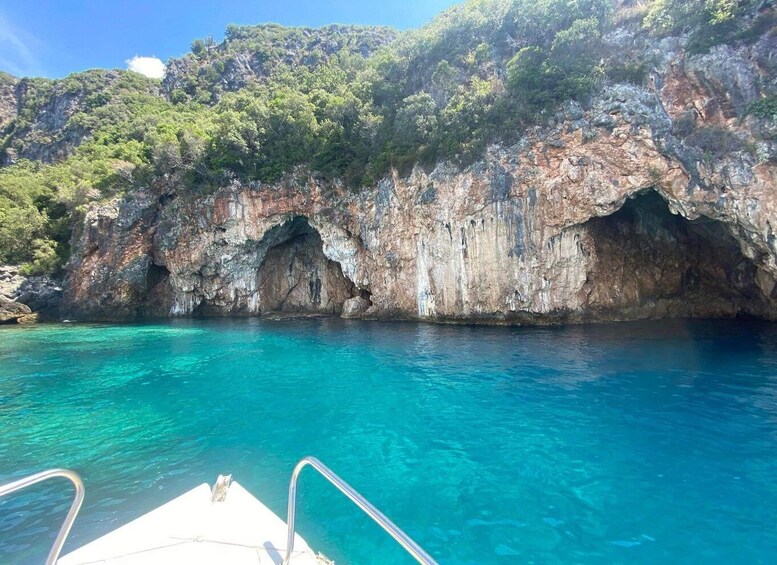 A boat near a rocky coastline with clear blue water and a forested hill. 3