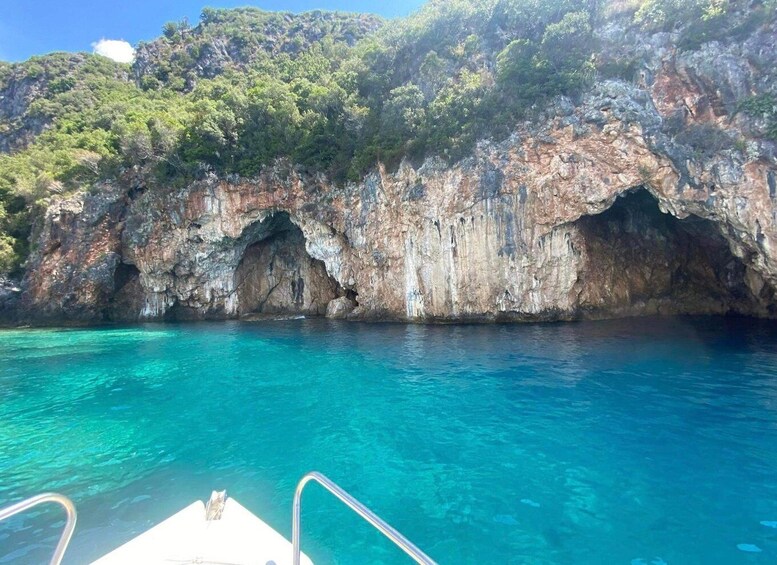 A boat near a rocky coastline with clear blue water and a forested hill. 4