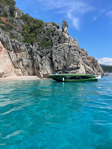 A green boat anchored near a rocky coastline with clear turquoise water. 1