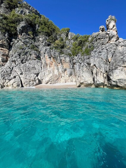 A coastal landscape with clear turquoise waters, rocky cliffs, and a sandy beach. 2