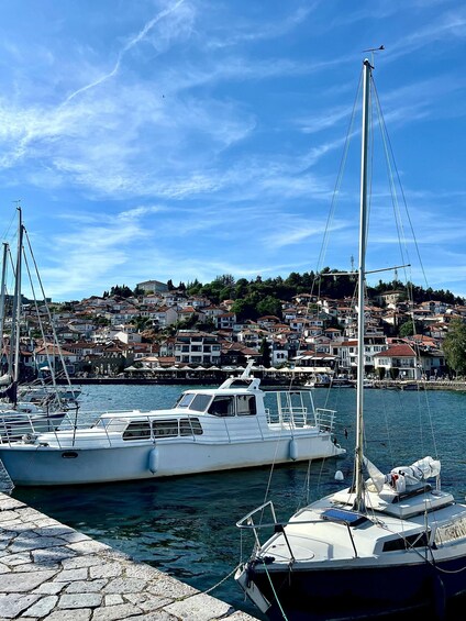 A harbor with boats docked, a clear sky, and a hillside of buildings in the background. 5