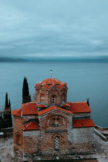 A historic church with red-tiled roofs and a bell tower, overlooking a calm body of water. 3