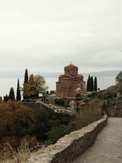 A historic church with a bell tower, surrounded by trees and a stone wall. 4
