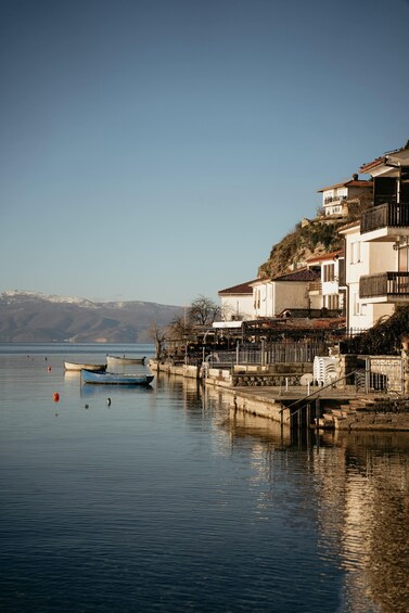 A calm lake with boats, a pier, and buildings on a hillside. 2