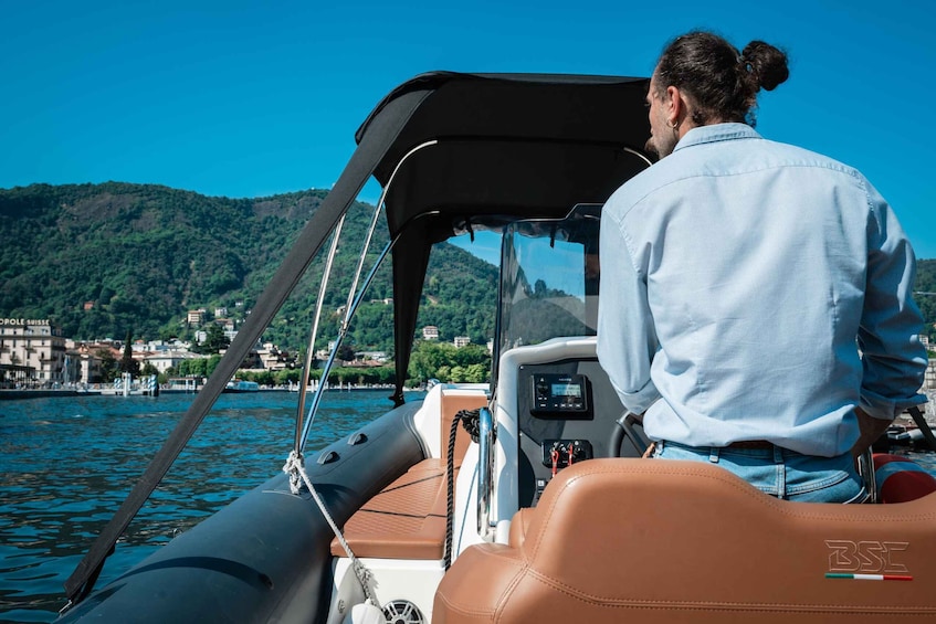 A man on a boat with a control panel, water, and a mountainous landscape in the background. 3
