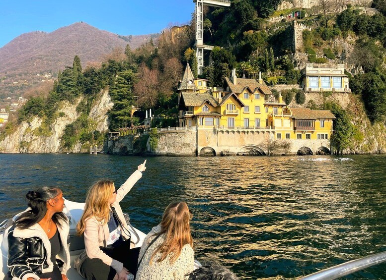 A group of people on a boat pointing towards a castle on a cliff by a lake. 1