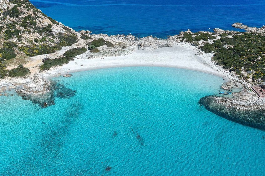 A turquoise beach with white sand, surrounded by rocky terrain and greenery. 4