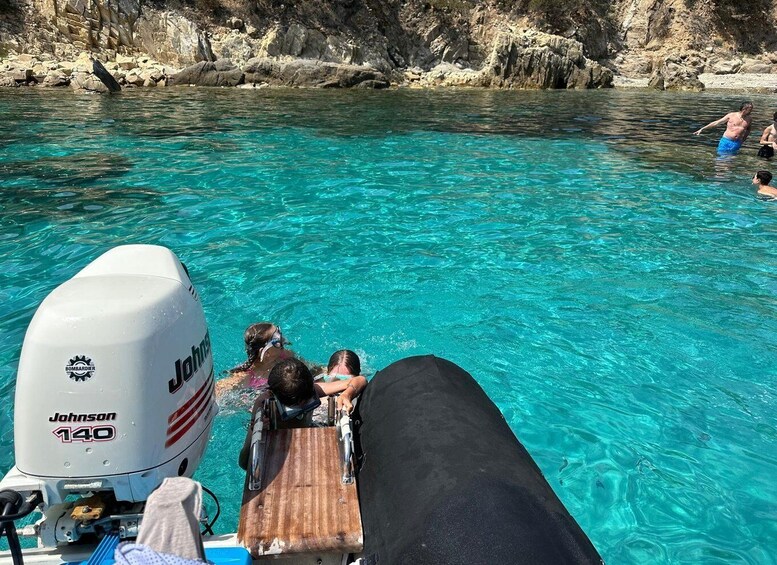 A boat with a Johnson 140 outboard motor, people swimming in clear turquoise water, and rocky cliffs in the background. 3