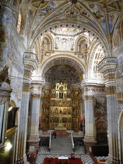 An ornate church interior with a high vaulted ceiling, detailed frescoes, and a central altar. 2