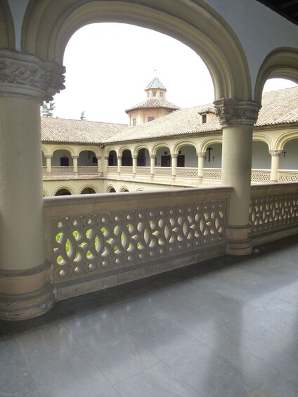 A courtyard with arches, a tiled roof, and a tower in the background. 5