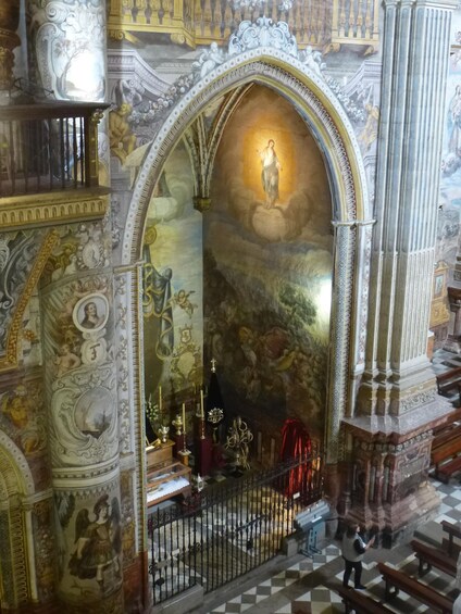 An ornate church interior with a central archway, religious statues, and detailed frescoes. 3