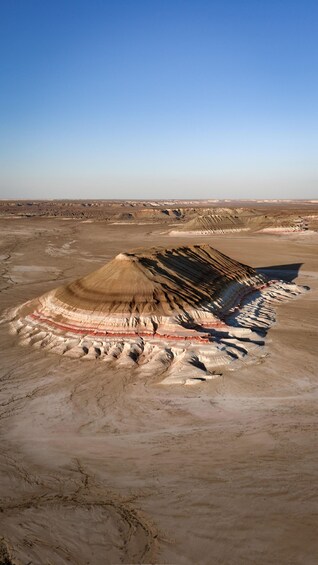 A large, flat, barren landscape with layered rock formations and a clear blue sky. 1
