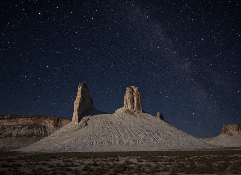 A desert landscape at night with a starry sky, two prominent rock formations, and sparse vegetation. 4