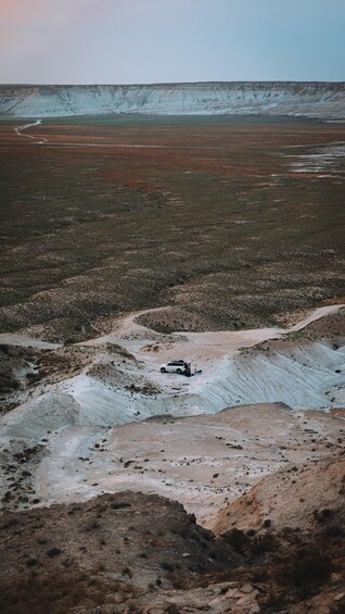 A barren landscape with a white vehicle parked on a rocky outcrop. 5