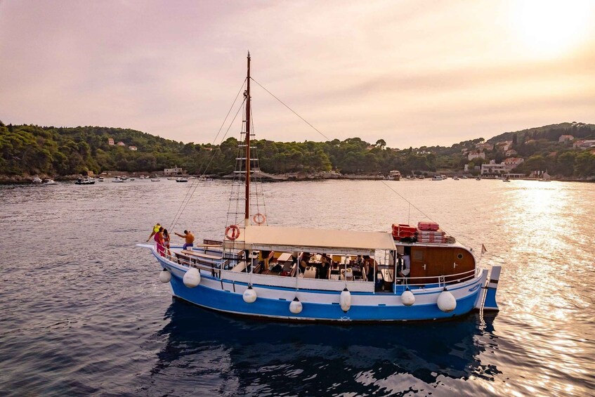 A blue and white boat with passengers on a calm body of water, surrounded by a hilly landscape with buildings in the distance. 2