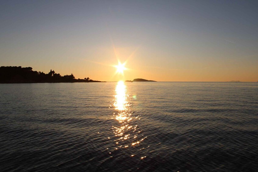 A sunset over a calm sea with a silhouette of a landmass on the left. 5