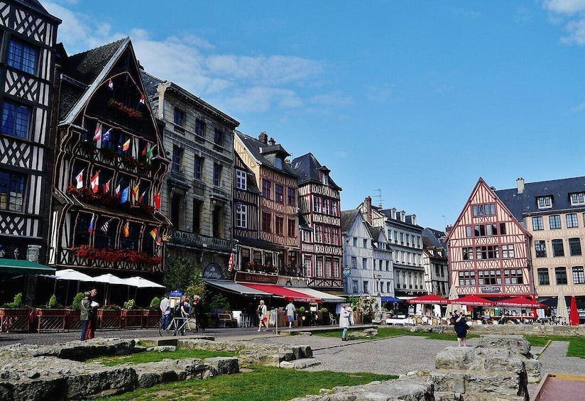 A historic European town square with traditional half-timbered buildings, cobblestone streets, and outdoor seating areas. 1