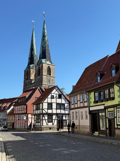 A cobblestone street with historic half-timbered buildings and a church with two spires. 2