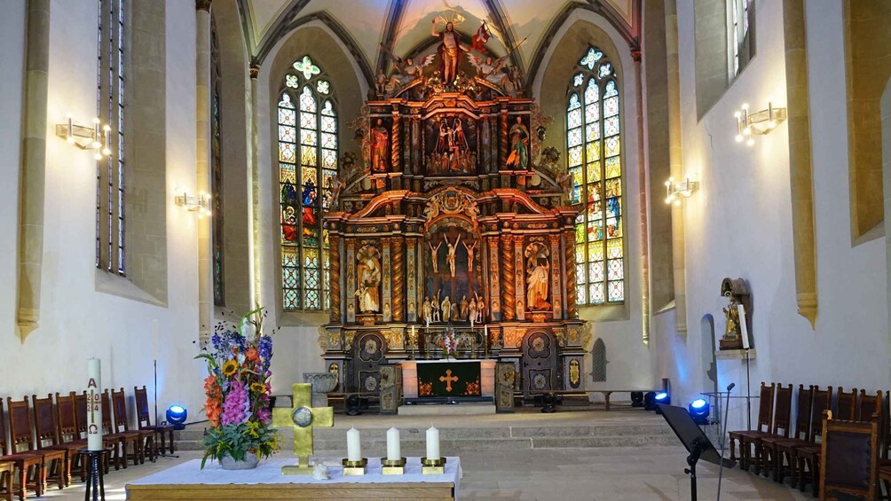 An ornate church interior with stained glass windows, a central altar, and rows of wooden pews. 3