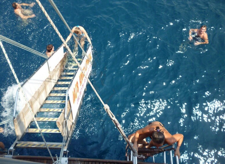 A boat with a ladder leading into the water, people swimming, and a sign with partially visible text. 5