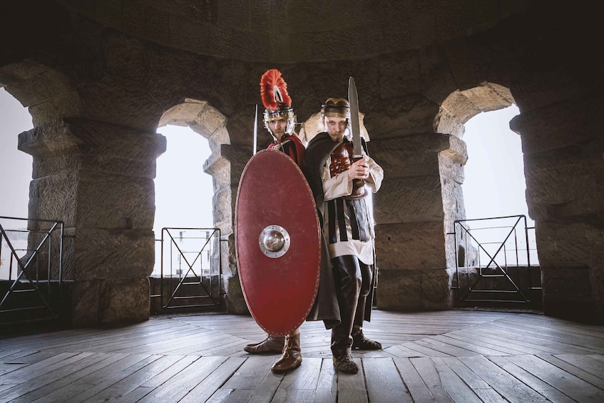 Two individuals in historical armor, one holding a shield and the other a sword, standing in a stone archway structure. 4