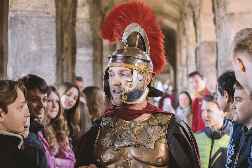 A person in a Roman-style helmet and armor, standing in a historical building with arches. 1