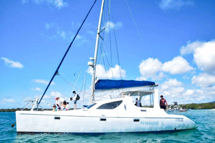 A sailboat named 'MARIANNE I' with people on deck, surrounded by clear blue water and a partly cloudy sky. 3