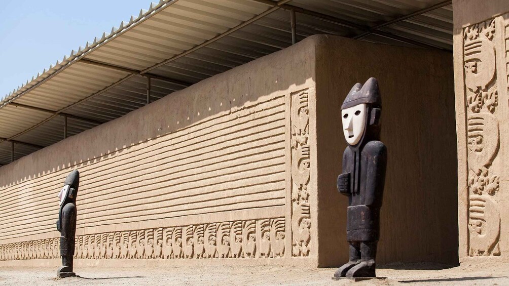 Un edificio grande con techo plano y una larga pared con figuras talladas. 4