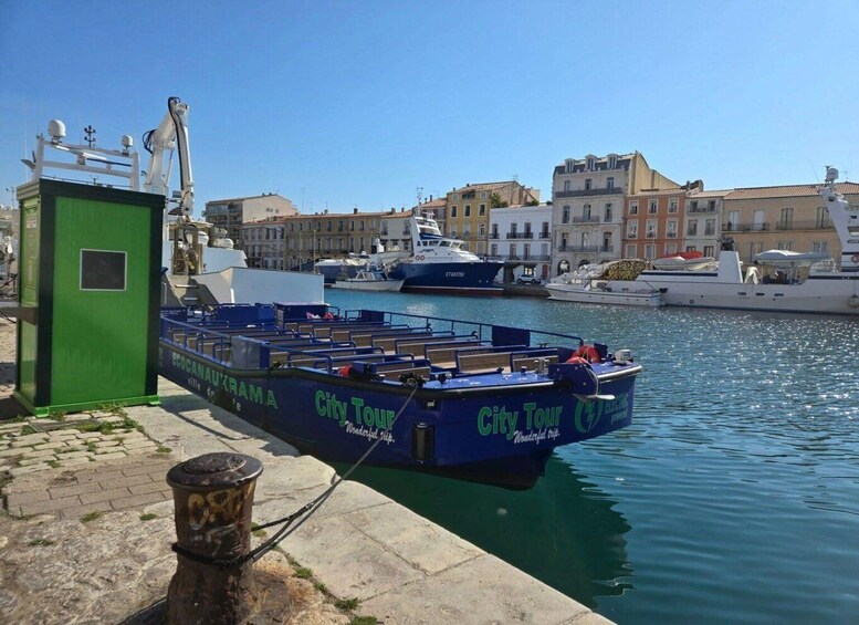 A blue boat docked at a marina with a city tour sign, a green structure, and buildings in the background. 3