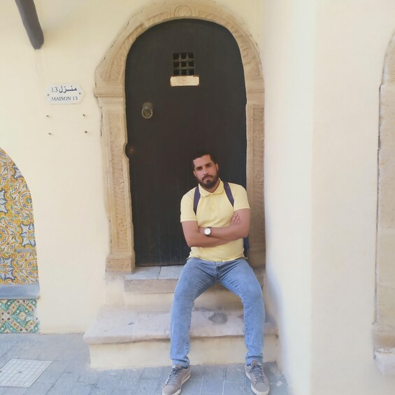 A man sitting on steps in front of a door with a sign above it. 4