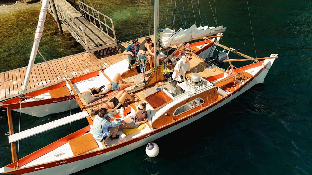 A small sailboat docked at a pier with people relaxing on the deck. 1